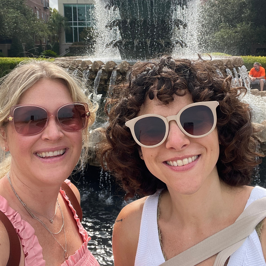 Best friends and moms traveling in Charleston. Standing in front of a fountain wearing sunglasses.